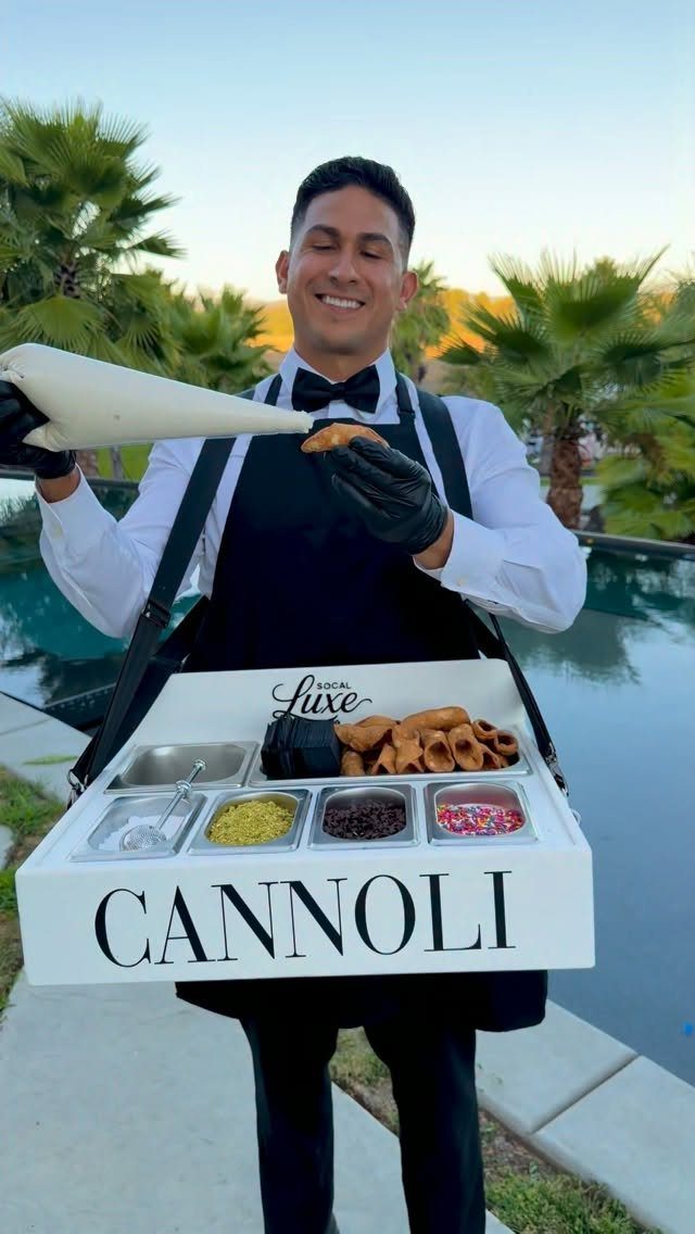 Man in formal attire filling cannoli from a portable dessert station outdoors