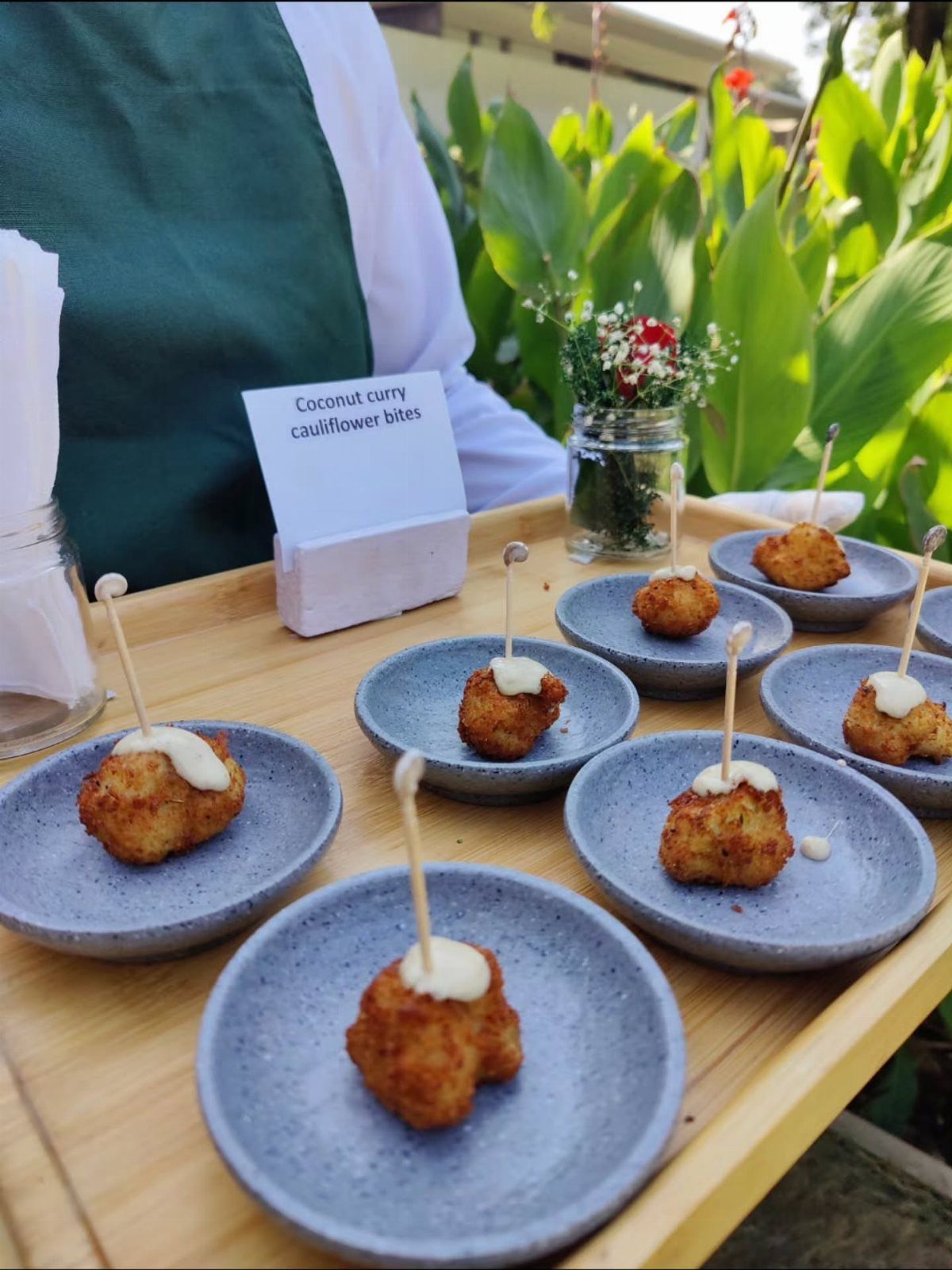 Coconut curry cauliflower bites on blue plates served on a wooden tray outdoors.