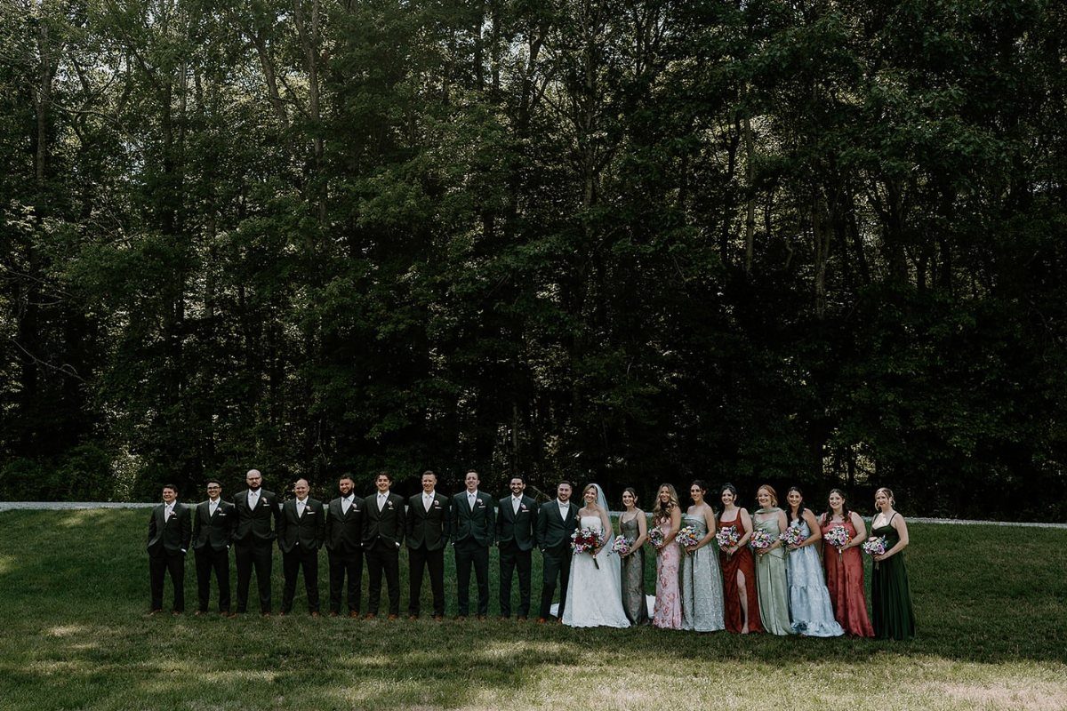 Wedding party posing in a line on grass against a forest background
