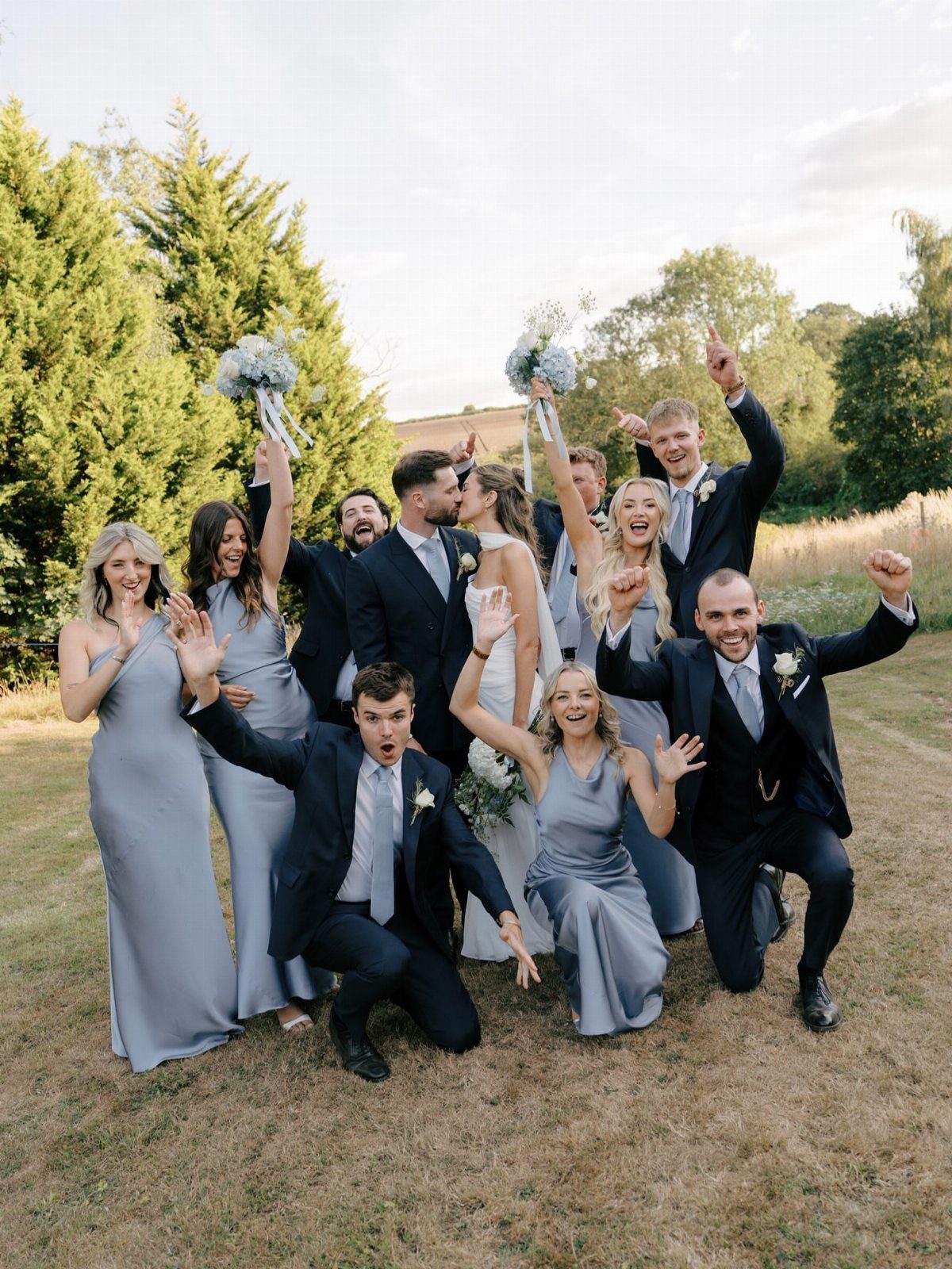 Wedding party cheering and laughing together outdoors in a grassy field.