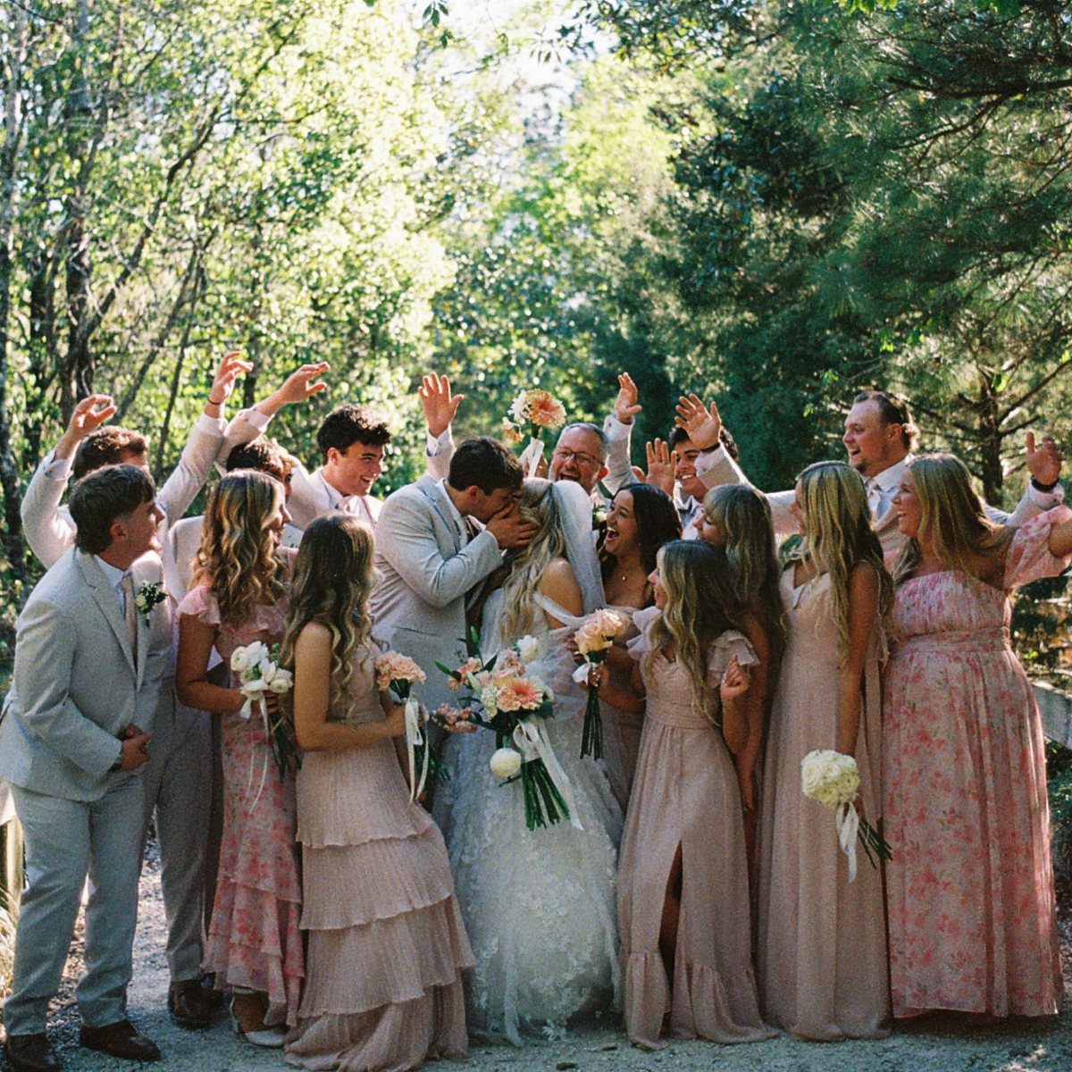 Bride and groom kissing while wedding guests cheer around them in a forest