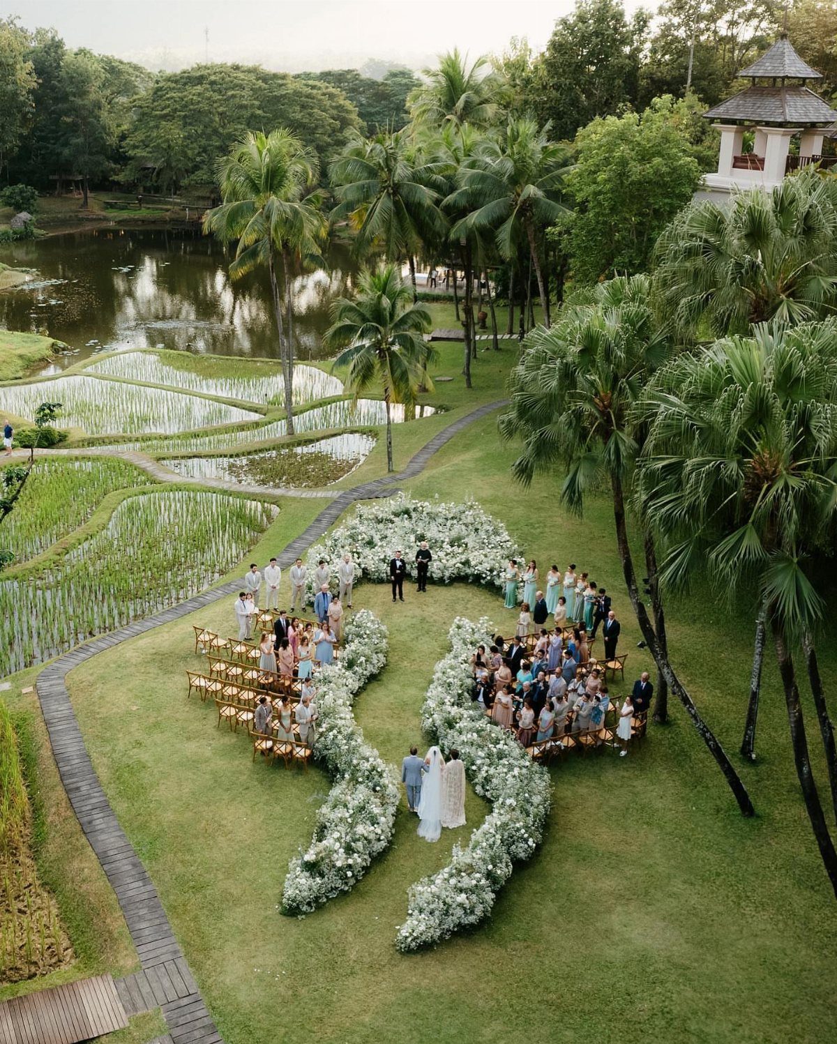 Aerial view of a wedding ceremony with guests and a floral aisle outdoors.