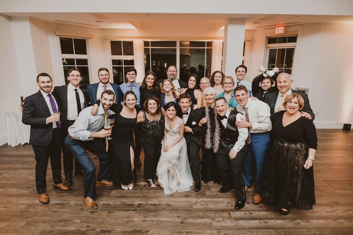 Large group of wedding guests and the couple posing in a white room.