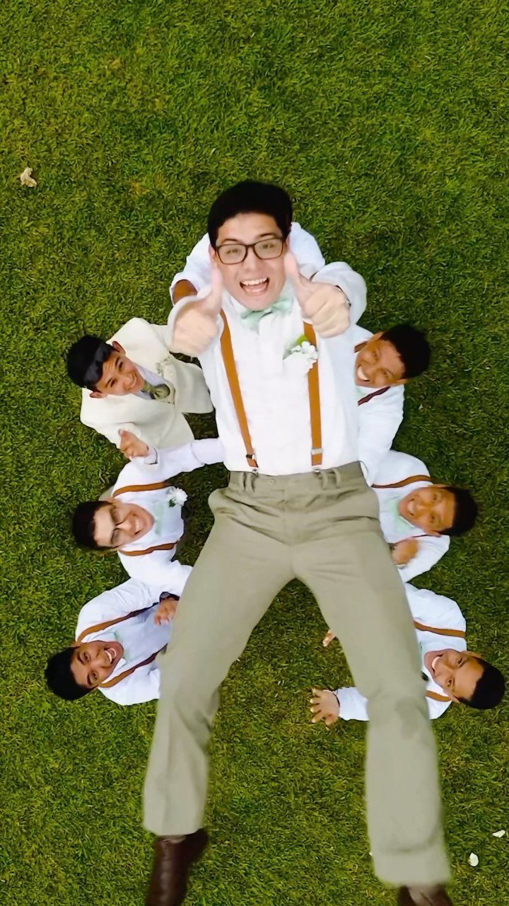 Groom and groomsmen posing creatively on a green lawn for a wedding photo