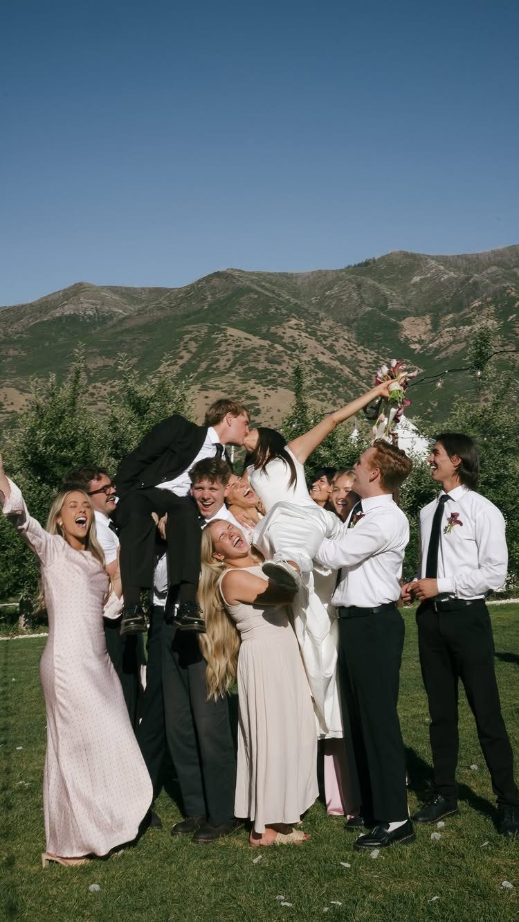 Wedding party lifting the groom to kiss the bride in a mountain setting.