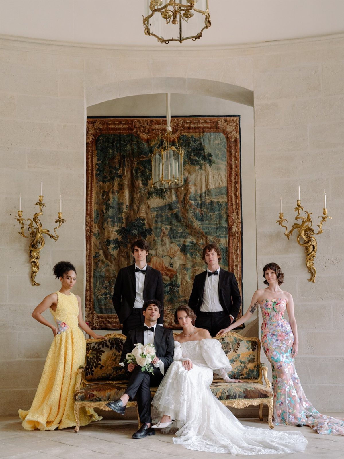 Wedding party posing formally in a room with a tapestry and ornate sofa.
