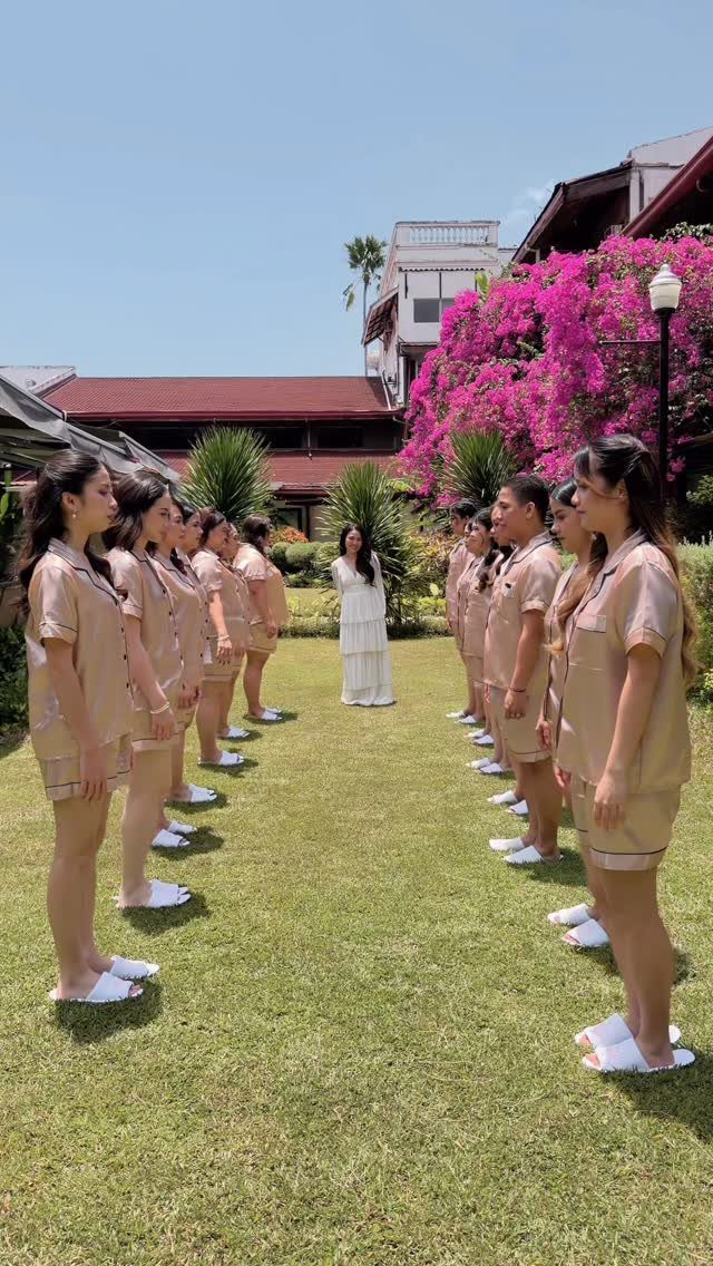 Bridal party in beige pajamas and bride in white dress posing on lawn