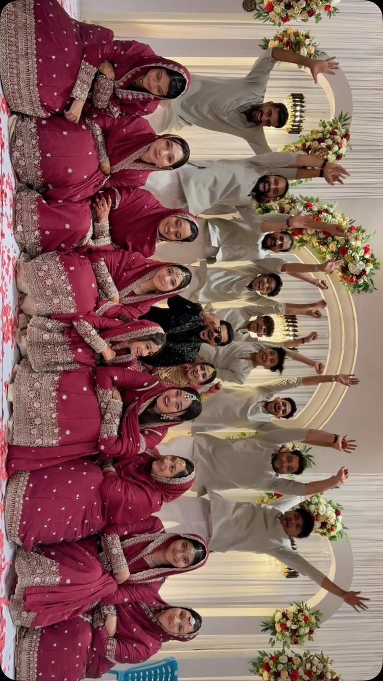 Group of wedding guests in maroon and white traditional attire posing together.