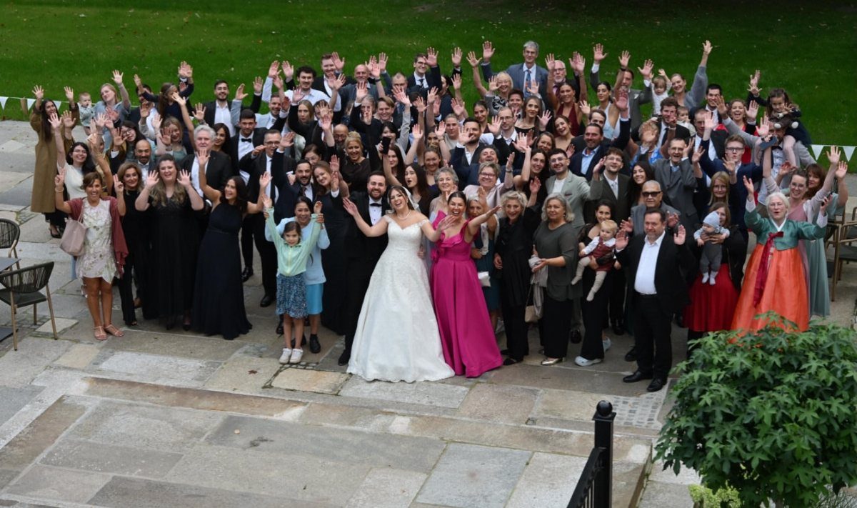 Bride and groom surrounded by a large group of waving wedding guests outdoors.