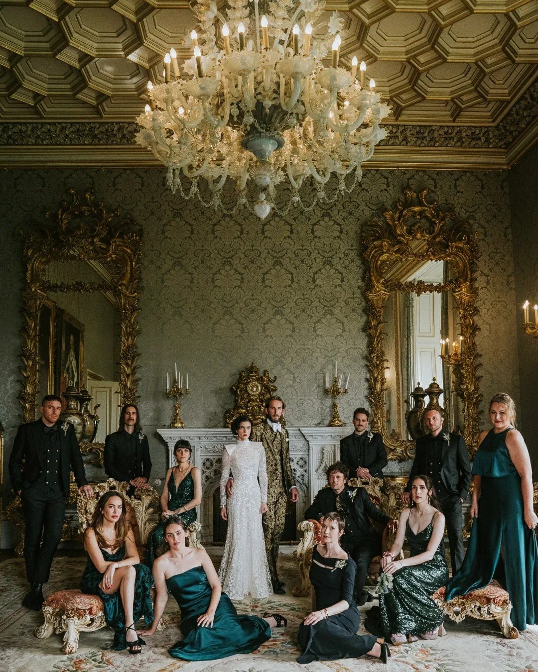 Wedding party posing in an ornate room with gold mirrors and a chandelier.