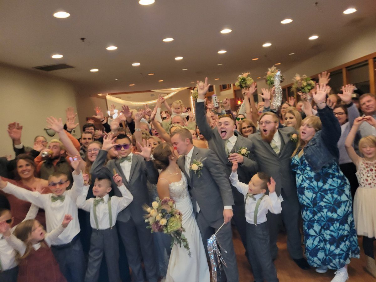 Wedding guests cheering with raised arms around a bride and groom in a hallway.
