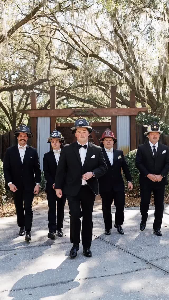 Five men in tuxedos and firefighter helmets walking toward the camera outdoors.
