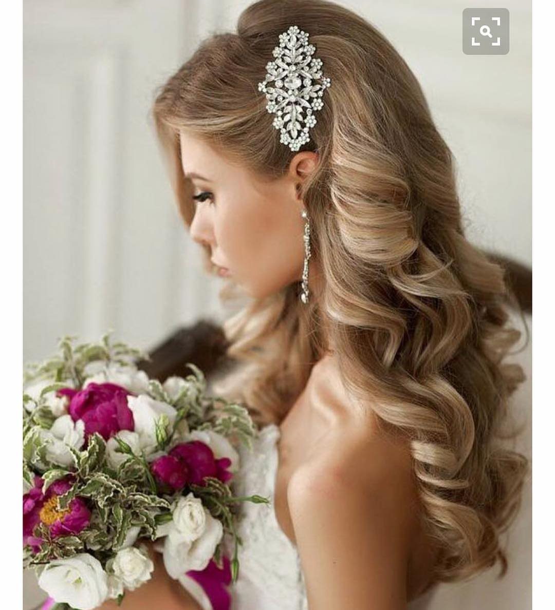 Blonde woman with side-swept curls, a silver hair accessory, and a floral bouquet.