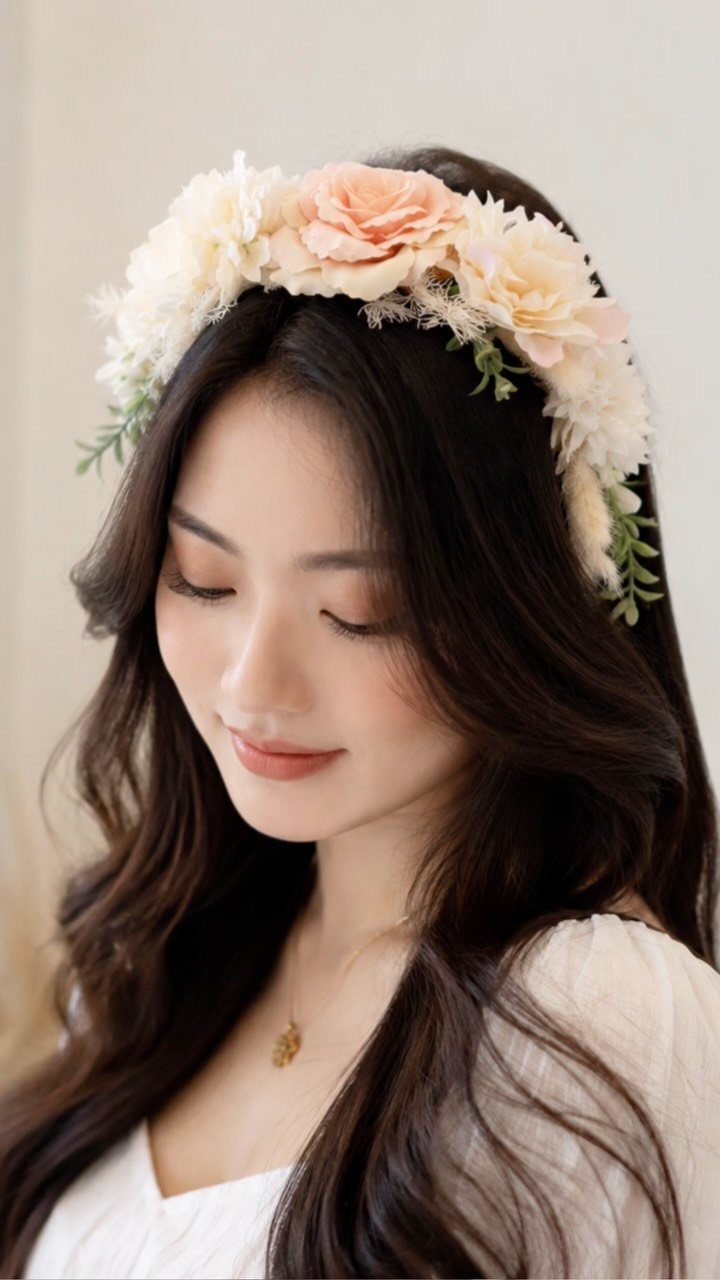 Woman with dark wavy hair wearing a peach and cream floral headband.