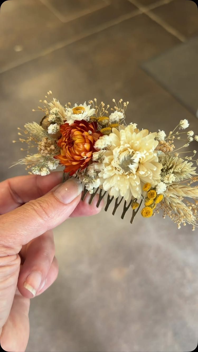 Hair comb decorated with orange and cream dried flowers held by a hand.