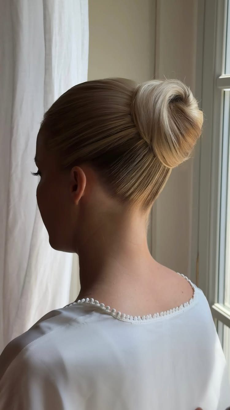 Blonde woman with a polished high ballerina bun and white beaded top.