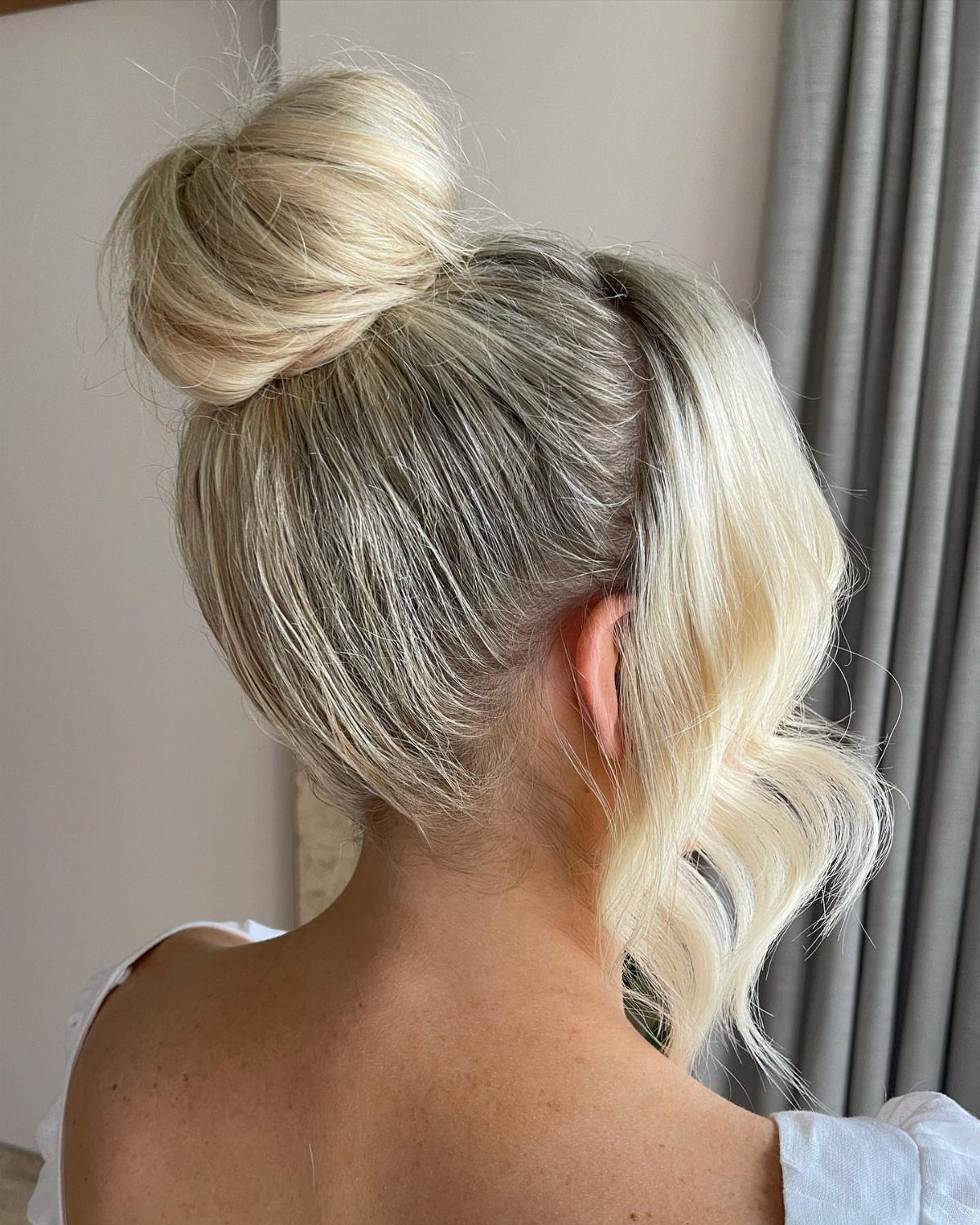 Blonde hair styled in a high casual knot with a loose wavy strand.