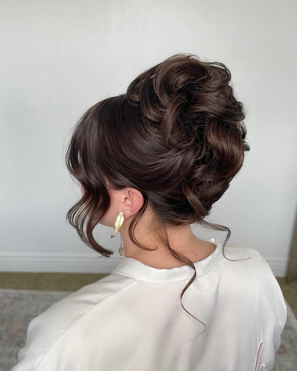 Woman with a voluminous curly brown updo and loose face-framing tendrils.