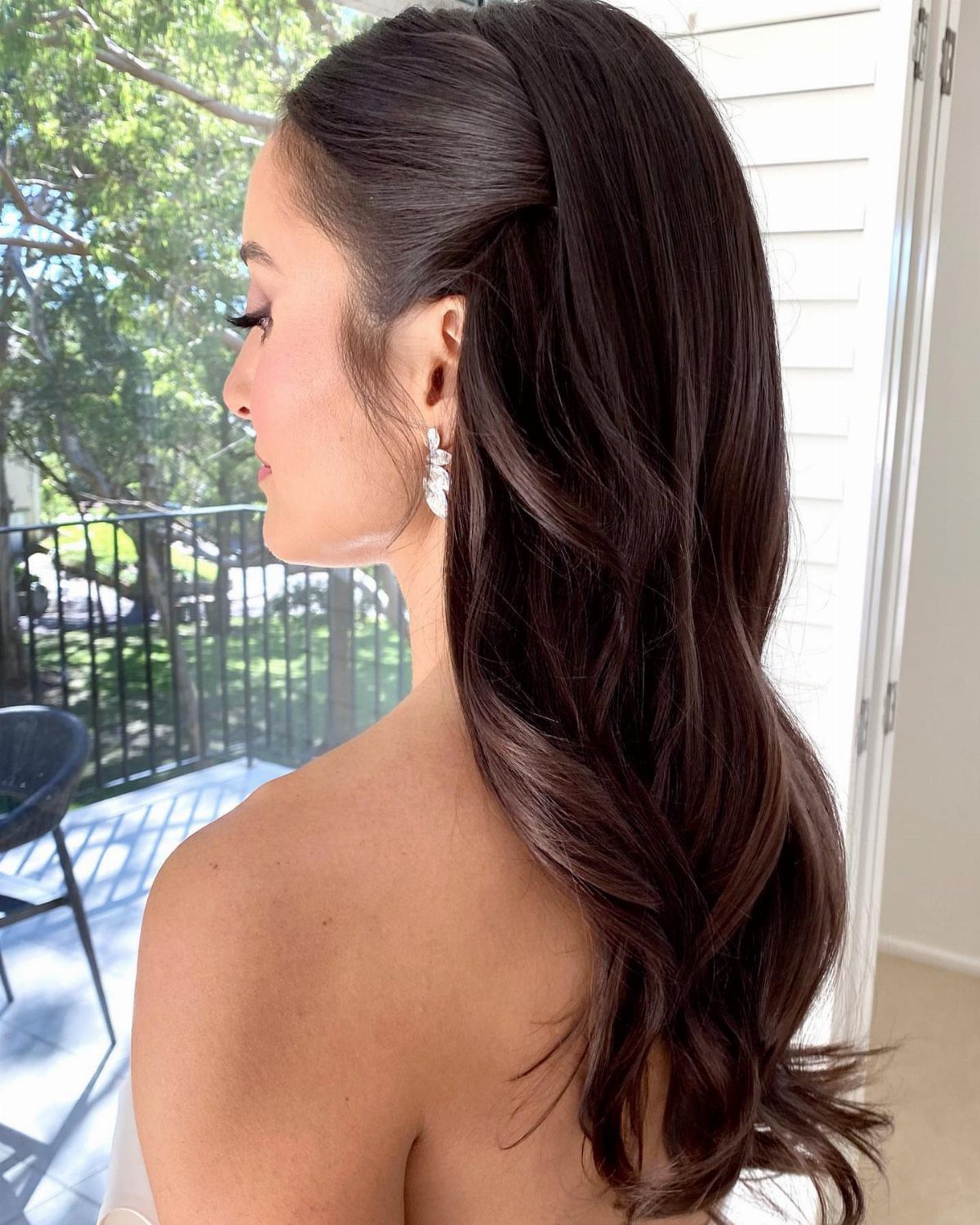Woman with dark brown wavy hair partially pinned back in a formal style.
