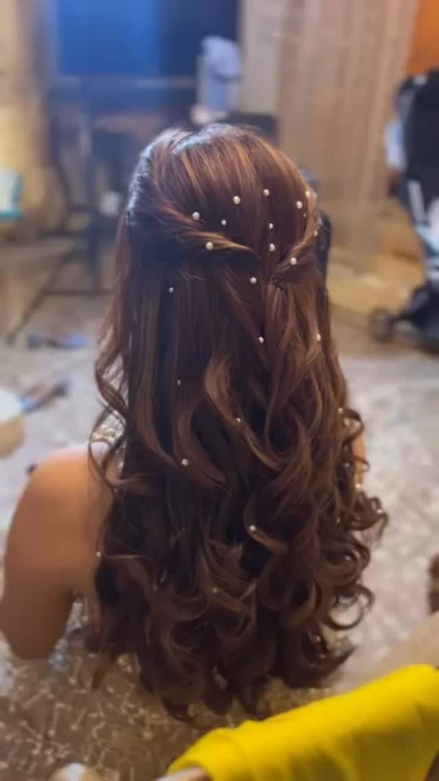 Curly brown hair partially pinned back and decorated with small white pearls.
