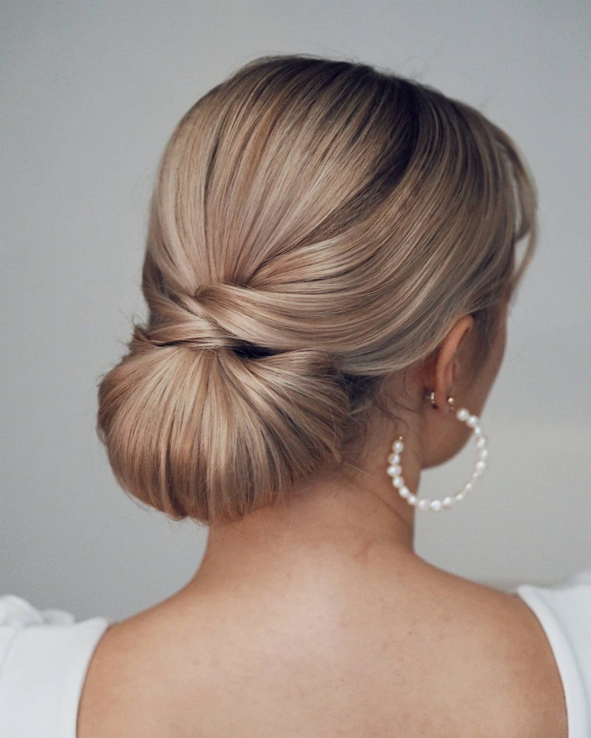 Blonde hair styled in a sleek low bun with pearl hoop earrings.