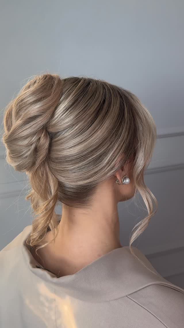 Blonde hair styled in a textured updo with loose curls and pearl earring.