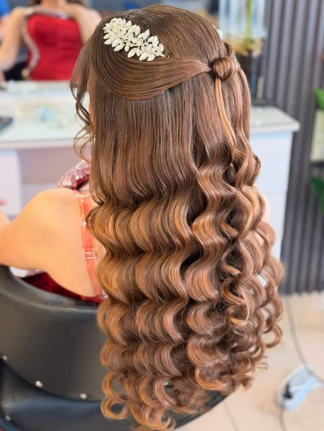 Long light brown hair styled in tight ringlet curls with a floral accessory