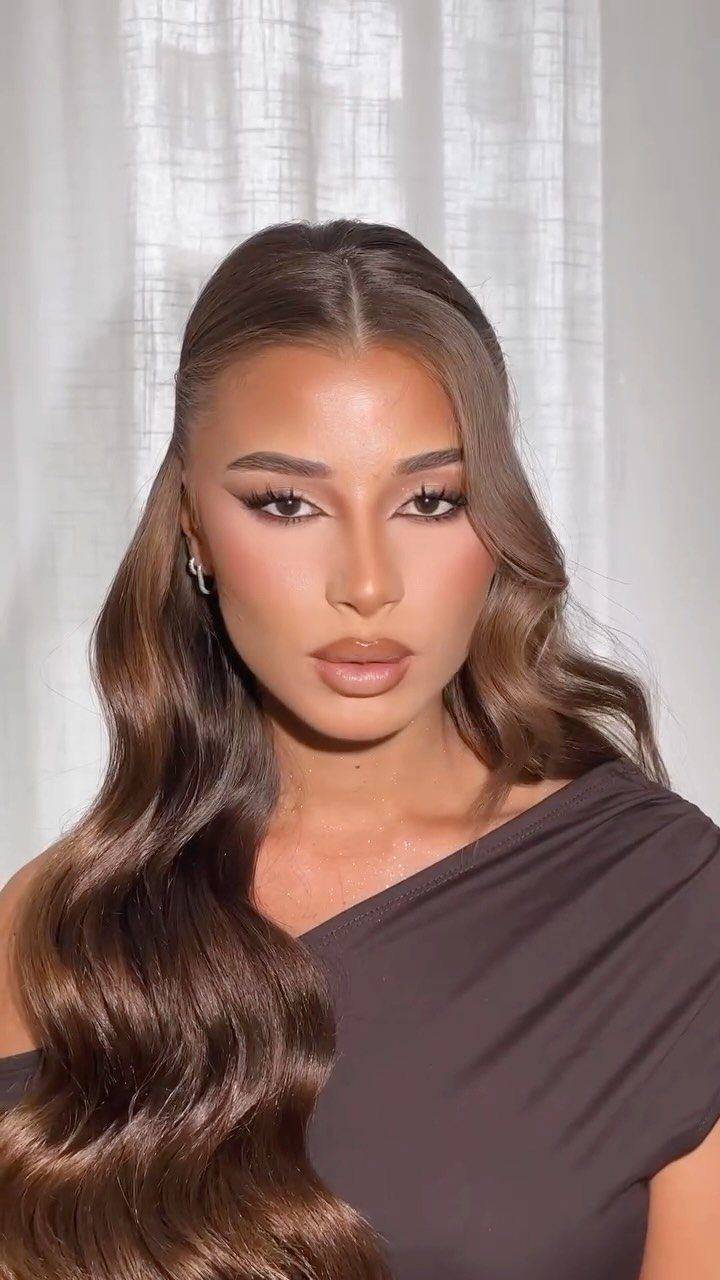 Woman with long brown hair styled in polished romantic waves and makeup