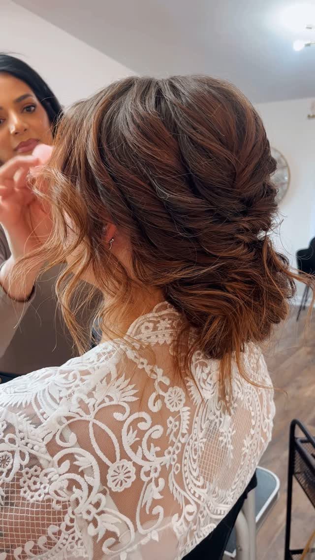 Brown hair styled in a textured low updo with white lace bridal dress