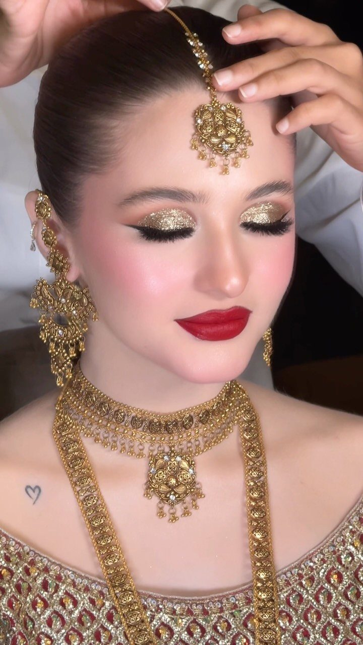 Woman with bold red lips and gold glitter eyeshadow wearing ornate gold jewelry