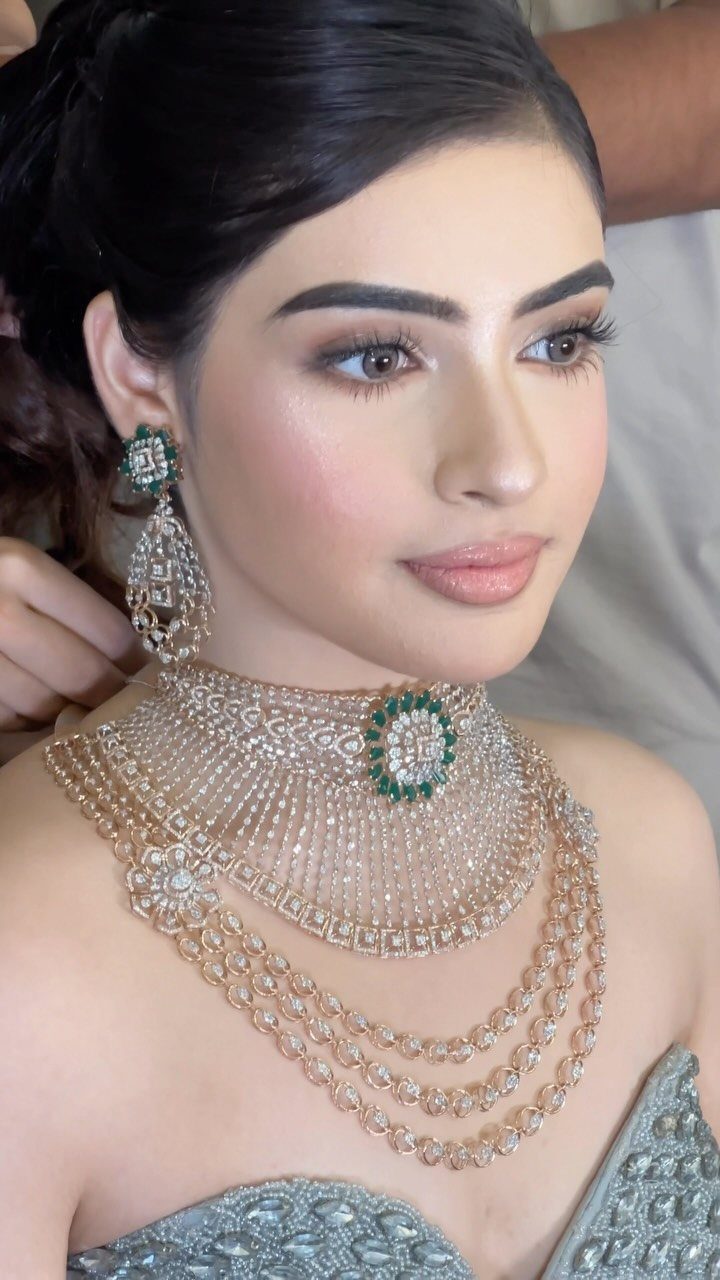 Woman with defined eye makeup wearing a lavish diamond and emerald bridal jewelry set.