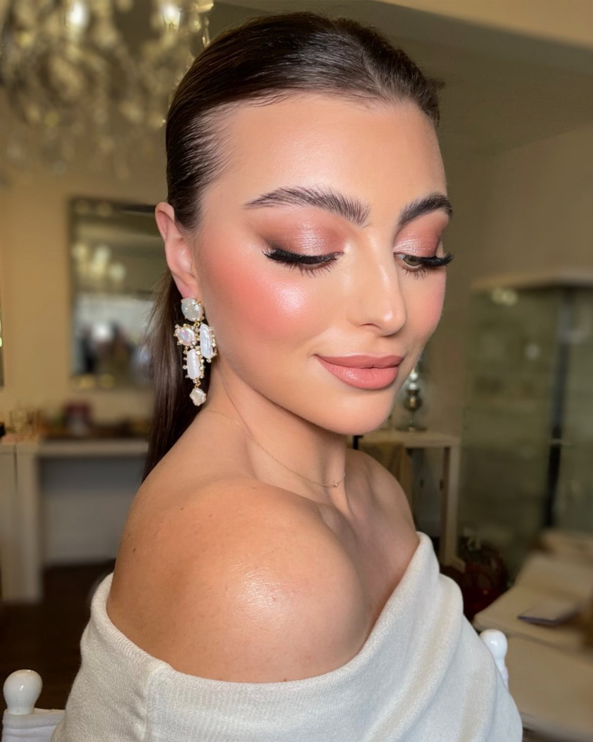 Woman with dusty rose eyeshadow, pink blush, and nude lips wearing white clothing.