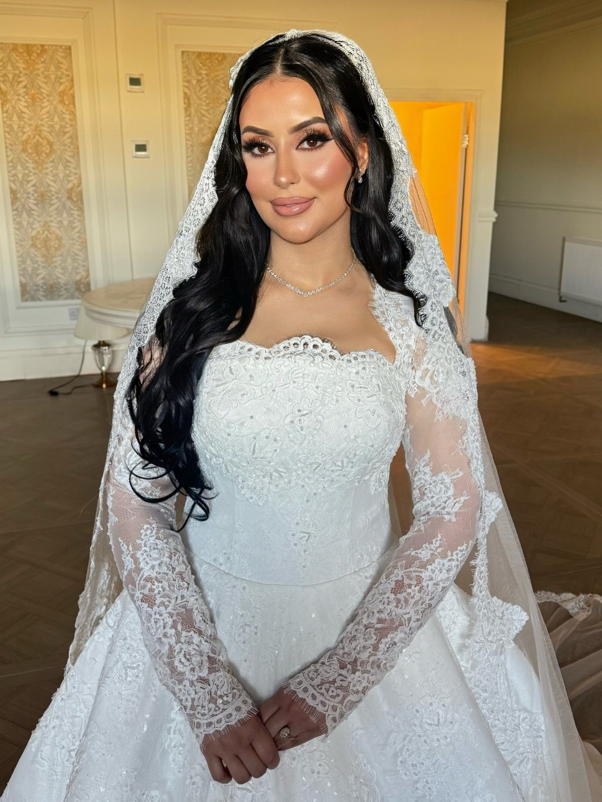 Bride in white lace gown and veil with voluminous lashes and glam makeup.