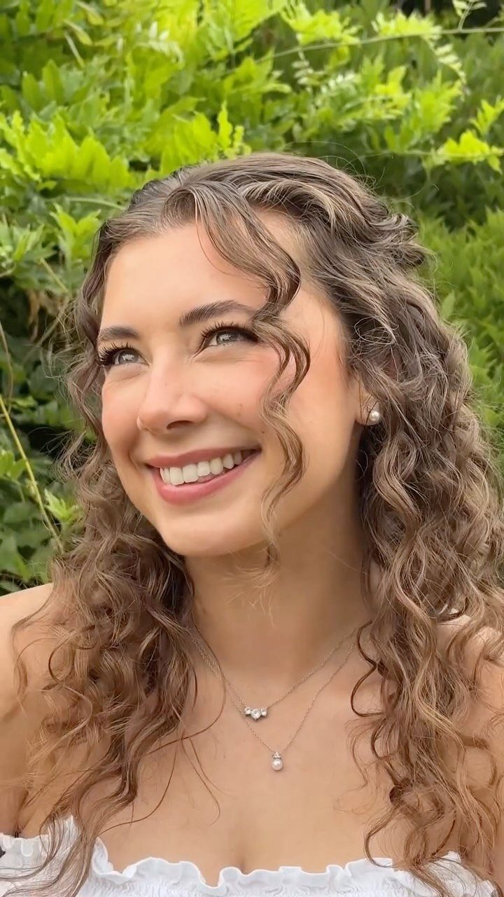 Smiling woman with curly brown hair wearing minimalist makeup and white ruffled clothing.