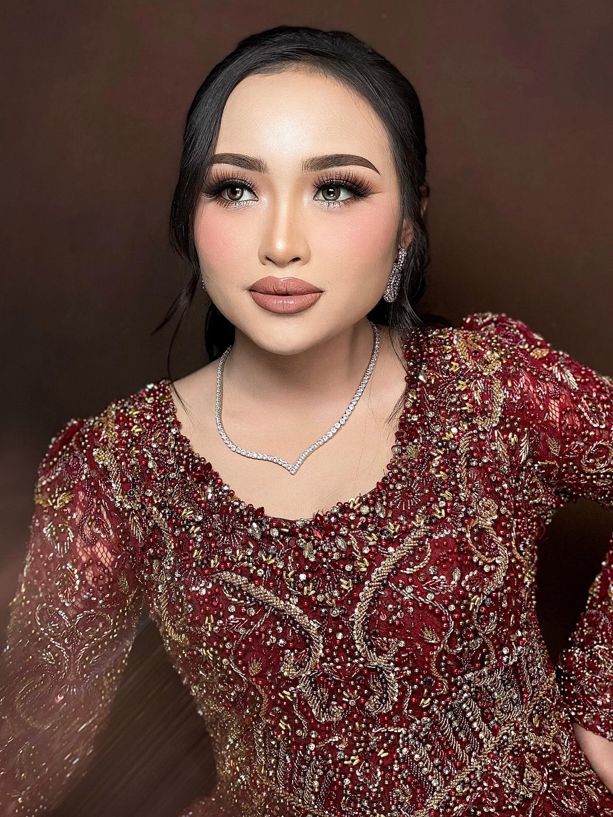 Woman with nude overlined lips wearing a red beaded gown and diamond necklace