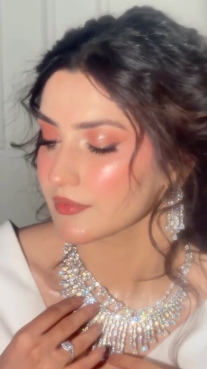 Woman with peach-toned makeup and diamond jewelry posing for a portrait