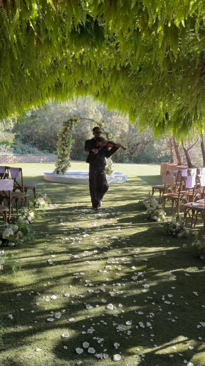 Violinist playing a violin at an outdoor wedding ceremony with white flower petals.