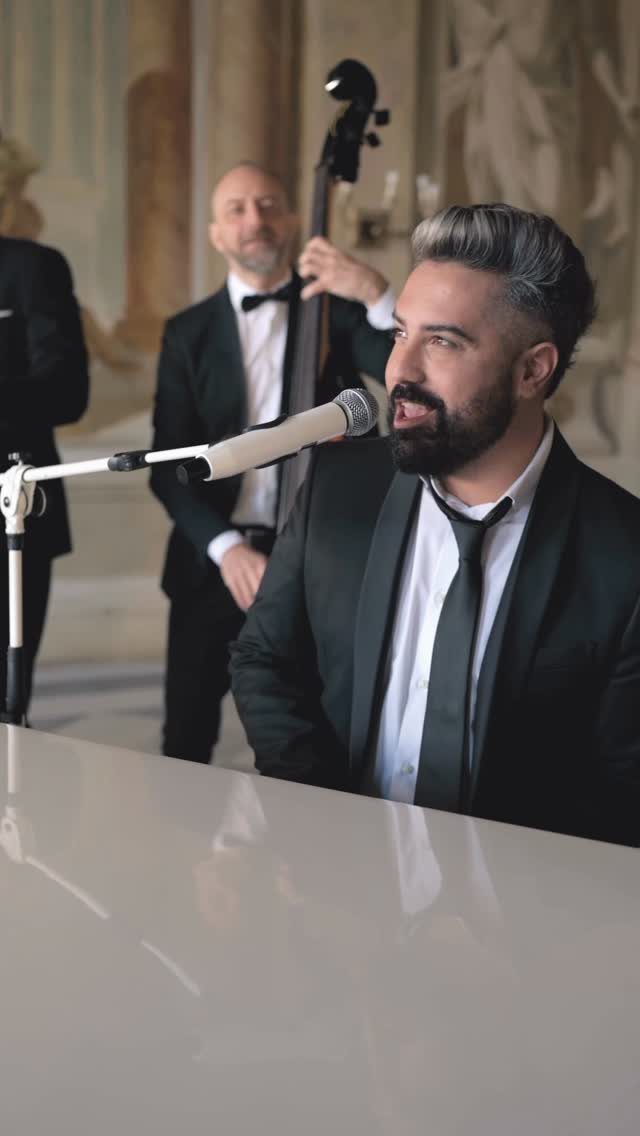 Male singer in a black suit performing with a double bass player indoors.