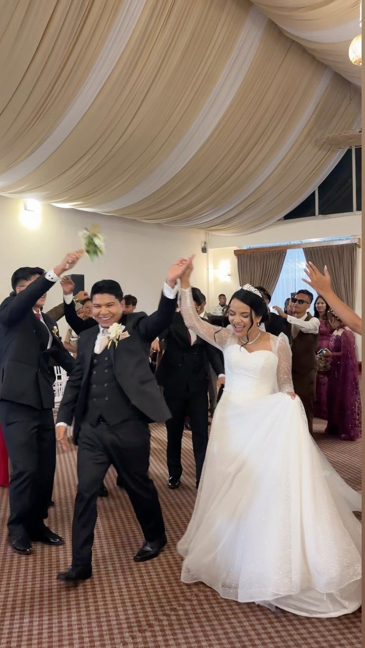 Bride and groom walking hand-in-hand into a wedding reception while guests cheer.