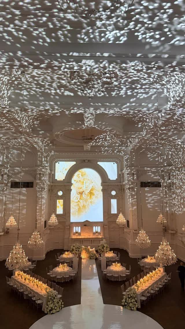 Grand white ballroom with ornate architecture, dappled lighting, and elegant wedding table settings.