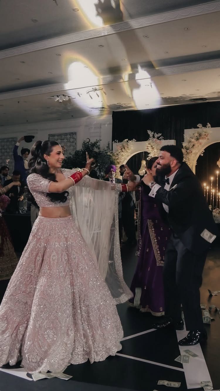 Couple dancing at a wedding, woman in pink lehenga and man in tuxedo.