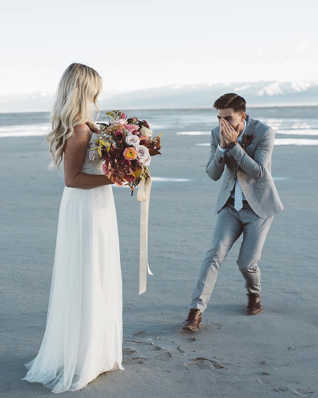 Groom reacting with surprise as he sees his bride on a sandy beach.