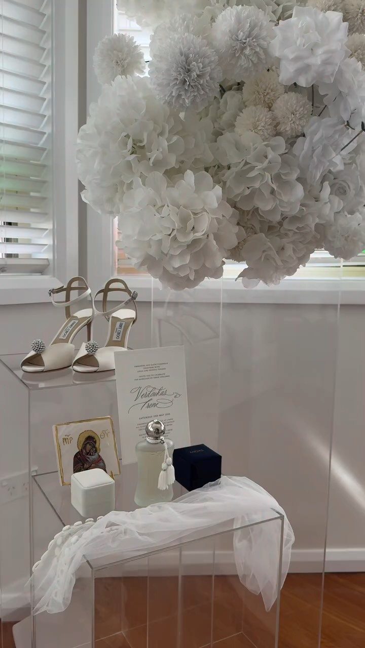 Bridal shoes, perfume, and white flowers arranged on clear acrylic display stands.