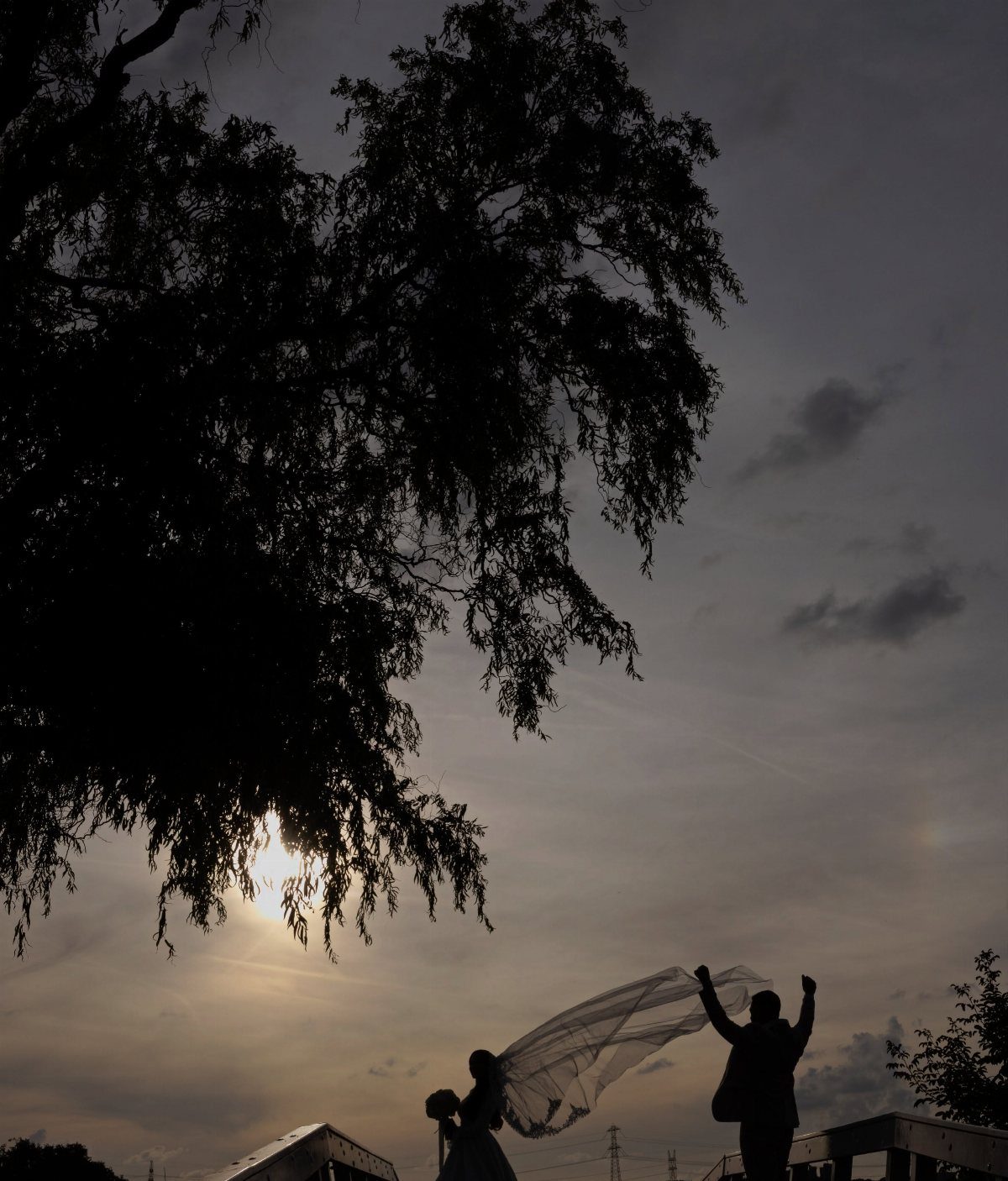 Silhouette of a bride and groom with a blowing veil against a sunset sky