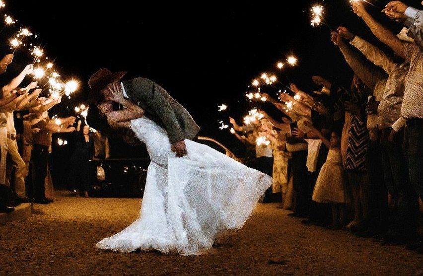 Bride and groom kissing during a sparkler exit at night surrounded by guests.