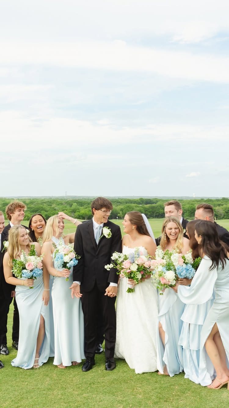Bride and groom holding hands surrounded by bridesmaids in blue and groomsmen in black.