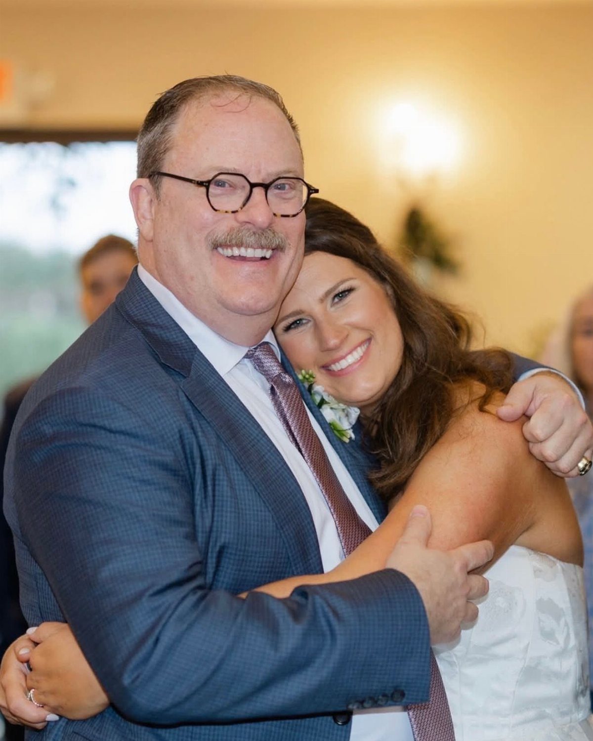 Smiling man in blue suit hugging a woman in a white wedding dress.