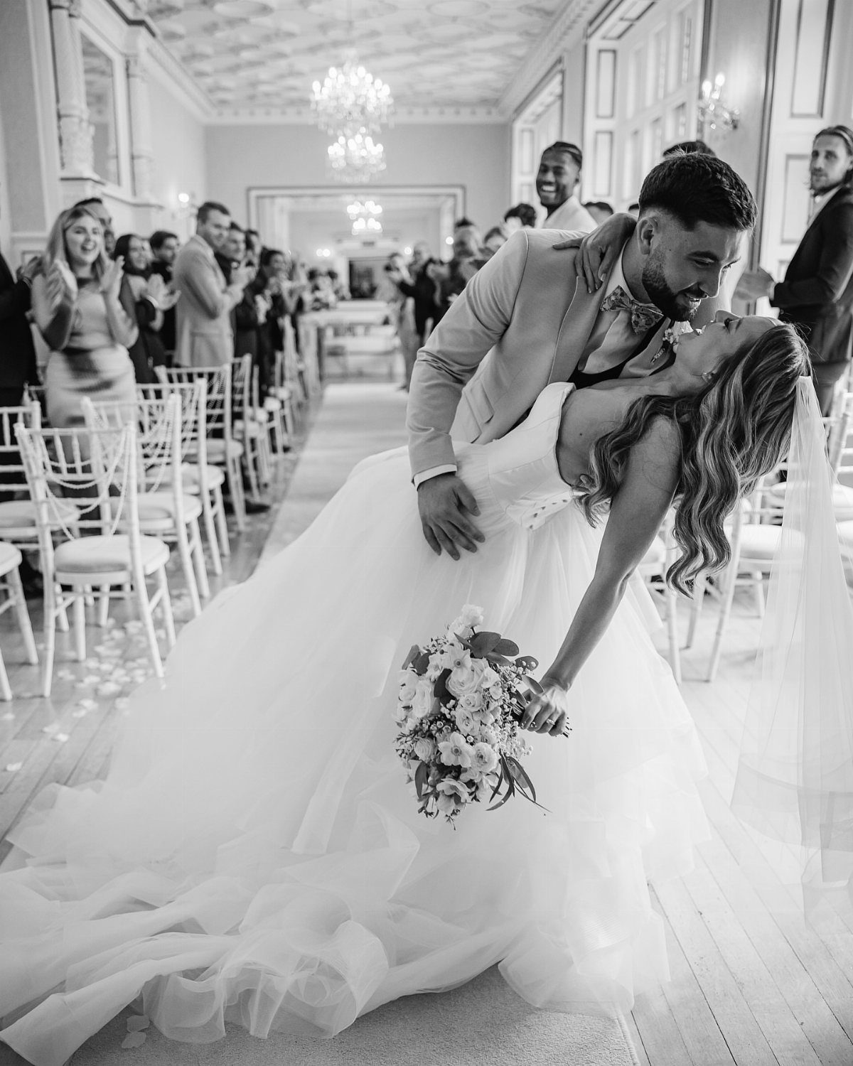 Groom dipping bride in a white wedding dress during a ceremony in a hall.