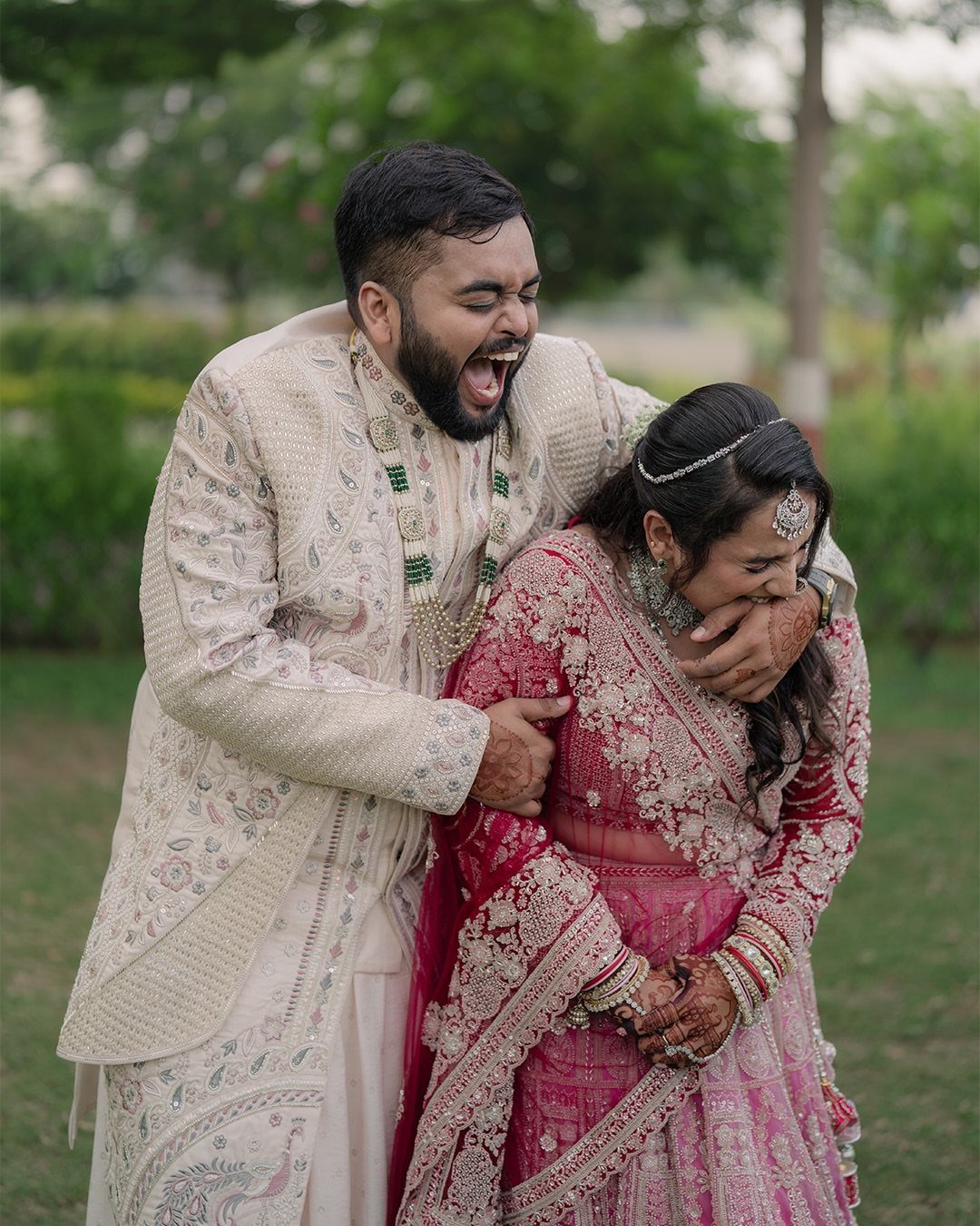 Indian wedding couple laughing together outdoors in traditional cream and red attire