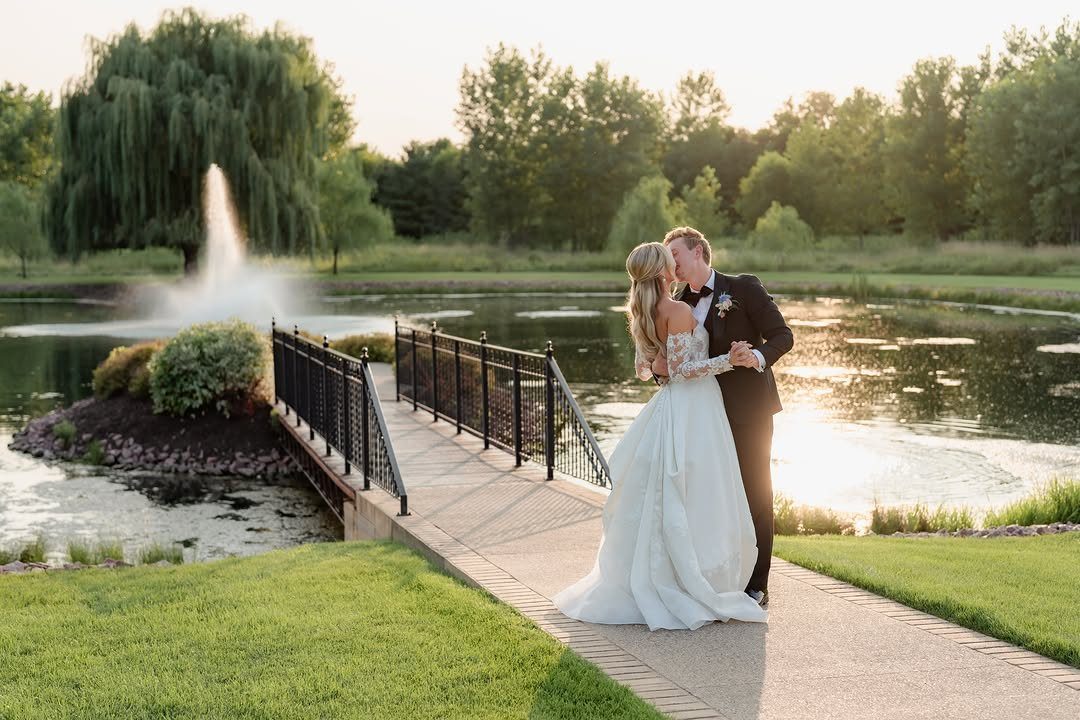 Bride and groom kissing on a bridge with a pond and fountain background